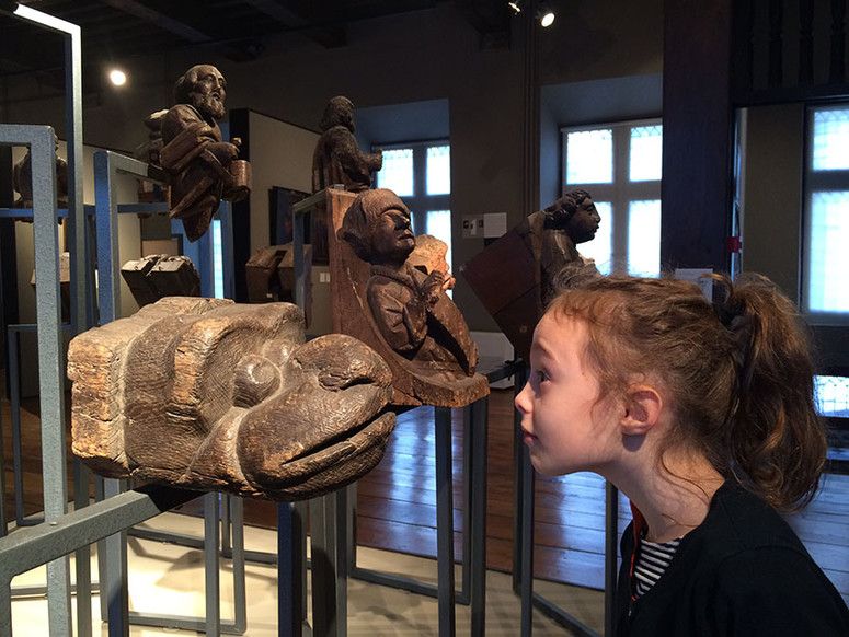 une petite fille devant un bois sculpté de tête de serpent
